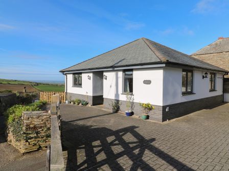 A white bungalow with potted plants on a paved area and countryside views at Chilowan in Trewarmett near Tintagel