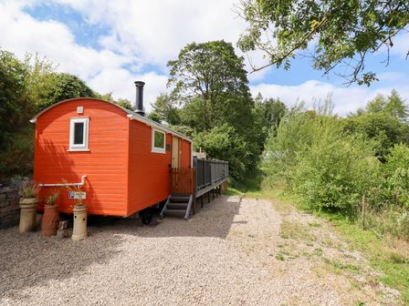 A shepherd's hut with a chimney and wooden steps in an outdoor area at Red Kite at Wild Valley Huts Llanrhaeadr-Ym-Mochnant