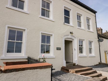 The exterior of a white two story house with multiple windows and a small set of steps leading to the entrance at Penny Bridge House in Ulverston