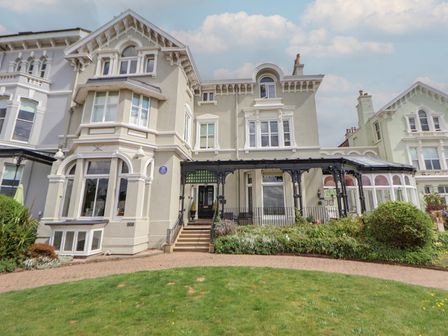 A large house with multiple windows and a covered porch with iron supports surrounded by a garden and lawn at Ismay Dining Room Suite - Titanic Interest in Waterloo Merseyside
