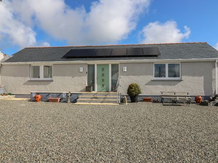A single story house with a green door solar panels on the roof and gravel in front at Brynteg Cottage in Tegryn