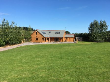 A wooden house with a grey roof surrounded by green lawn and trees at Riverside Lodge in Washford