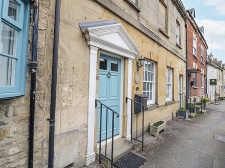 A row of houses with stone and brick walls blue doors and windows and small planters on the sidewalk at Lower Pack Horse Cottage in Winchcombe
