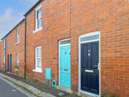 A row of brick houses with blue and turquoise front doors and white windows on a street at Chapelhay Cottage in Weymouth