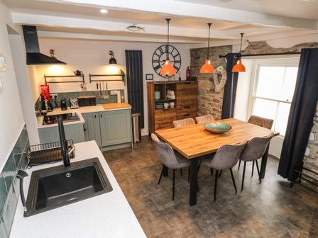 A kitchen and dining area with a wooden table and six chairs under orange pendant lights at Winterbrook Cottage in Mevagissey