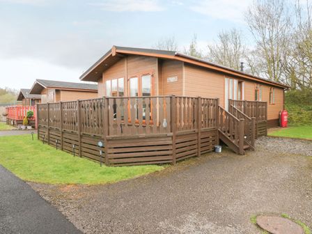 A brown wooden cabin with a fenced deck and steps on a grassy plot at Walkers Rest in Warton near Carnforth