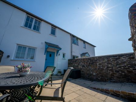 An outdoor patio area with a round metal table and chairs in front of a white building with blue doors at Oyster Cottage in St Ann's Chapel