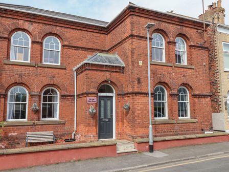 An exterior view of a two-story brick building with arched windows and a black door with hanging flower baskets at The Old Station House in Withernsea