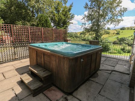 An outdoor hot tub with wooden paneling and steps on a paved patio with a view of green hills at Hillside Lodge in Newtown