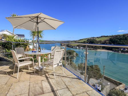 An outdoor patio with a table, four chairs, an umbrella, and a view of water and hills at 2 Channel View in Salcombe