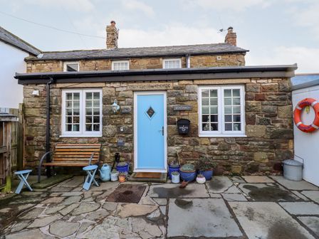 A stone house with a blue door and two windows a bench and flower pots outside at Seahares in Seahouses