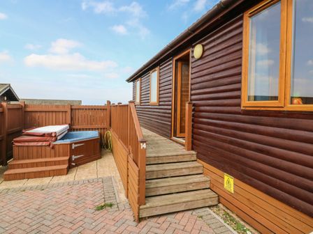 An exterior view of a wooden cabin with stairs leading to an open door next to a hot tub on a paved area at Seascape Retreat in Ilfracombe