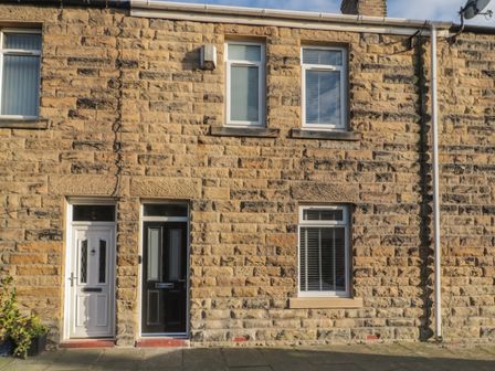A stone house exterior with a black door a white door and three windows at 55 Wellwood Street in Amble