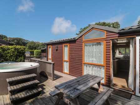 A wooden outdoor deck with a picnic table and hot tub outside a brown cabin at Birch in Swanage