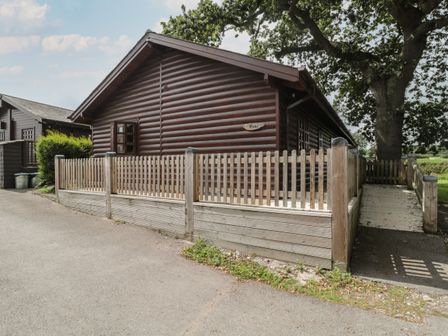 A wooden cabin with a fenced porch and a ramp leading to the entrance at Oaks in Swanage
