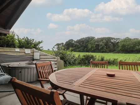 An outdoor patio with a wooden table and chairs next to a hot tub overlooking a green field at Walnut in Swanage