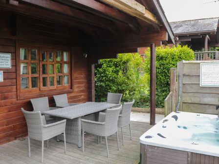 An outdoor covered seating area with a table and six chairs next to a hot tub at Pine in Swanage