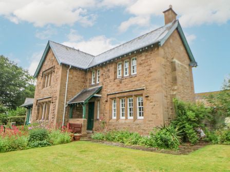 A stone house with multiple windows and a small garden with flowers and shrubs at Crookham Dairy in Crookham near Etal