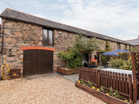 Exterior view of a stone building with wooden doors and windows a patio area with plants and umbrellas at Foxglove Barn in South Brent