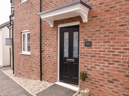 A front door of a brick house with a small potted plant and a white canopy above the door at Conybeare Cottage in Lyme Regis
