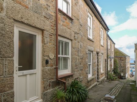 A stone building with white door and windows along a narrow cobblestone street near the water at Bodillys Cottage in Newlyn