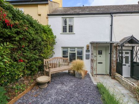 A small garden area with a wooden bench and potted plants outside a cottage with green windows and a covered front door at Holly Cottage in Lyme Regis