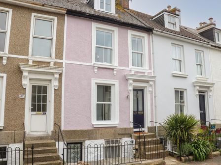 A row of terraced houses with stairs leading to front doors and windows on a residential street at The Lookout in Penzance