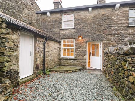An outdoor stone courtyard with stone walls stone flooring and two white doors at Hazelrigg Cottage in Newby Bridge