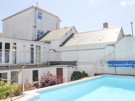 A backyard with a swimming pool and white buildings in the background at Topside in Salcombe