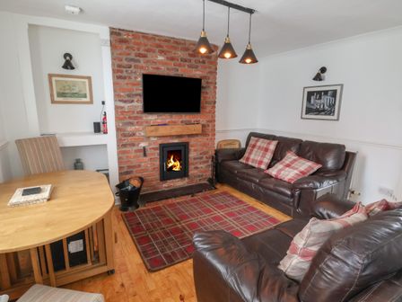 A living room with two leather sofas a brick fireplace with a fire a wooden table and a patterned rug at Ty Pen Y Bryn in Conwy