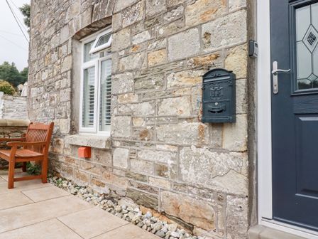 A stone wall exterior with a window a wooden bench a black mailbox and a dark blue door at Still Waters in Pentewan
