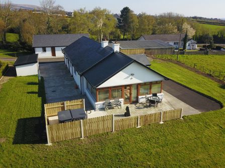 A single-story house with a fenced patio area and outdoor furniture in a rural setting at Rose Cottage in Muff County Donegal