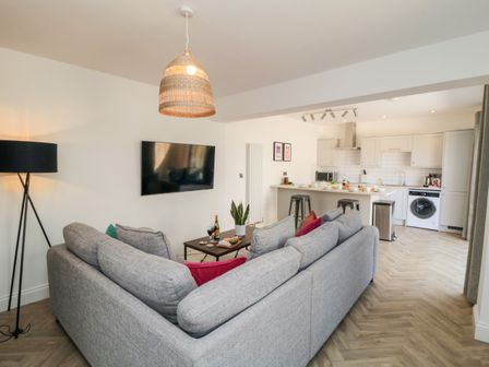 An open living room and kitchen with a gray sofa a coffee table a wall-mounted TV and kitchen appliances at The Salthouse Apartment 1 in Scarborough