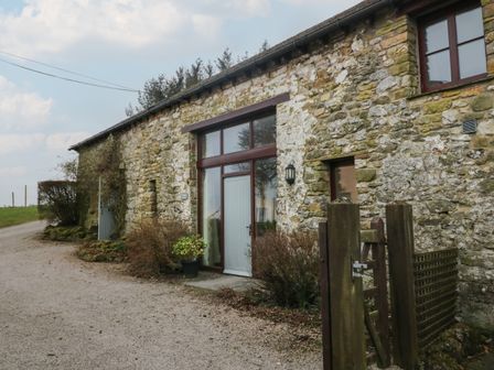 Stone barn exterior with a wooden gate gravel driveway and potted plants at Winder Barn in Askham Cumbria