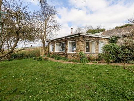A stone house with large windows surrounded by grass and trees at Eweleaze in West Bexington