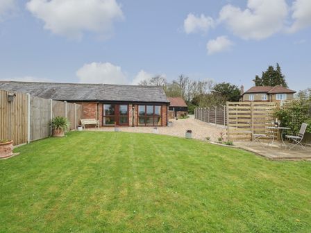 A lawn garden with potted plants and patio furniture in front of a brick building at Bee Happy Barn in Beighton near Acle