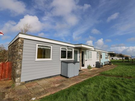 An exterior view of a single story building with windows a door a storage box and benches on a grassy area at Nanny's Little House in Sandown