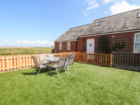 A fenced garden area with a table and six chairs outside a brick cottage at Oak Cottage in Dinas Dinlle near Caernarfon