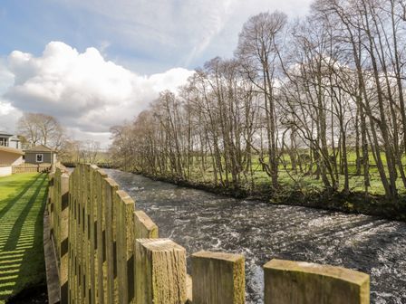 A river flowing alongside a wooden fence with trees and green grass at Mill End in Eamont Bridge near Penrith