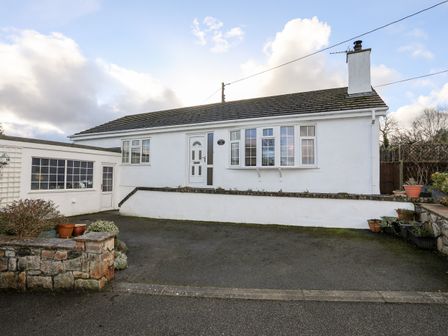 A white single-story house with a driveway and potted plants at Neaudd Wen in Red Wharf Bay near Benllech