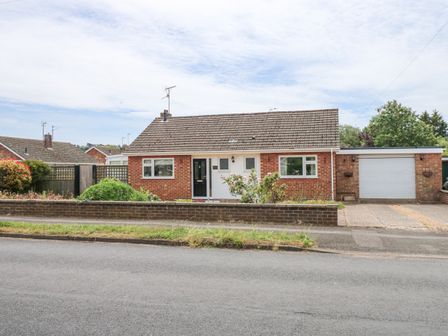 A single-story brick house with a tiled roof a black front door two windows a driveway and a garage at Potters Retreat in Dersingham