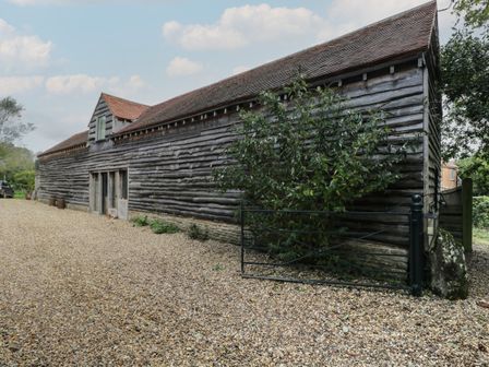 An exterior view of a long wooden barn with a tiled roof and gravel driveway at Brandeers Long Barn in Brandier near Minety