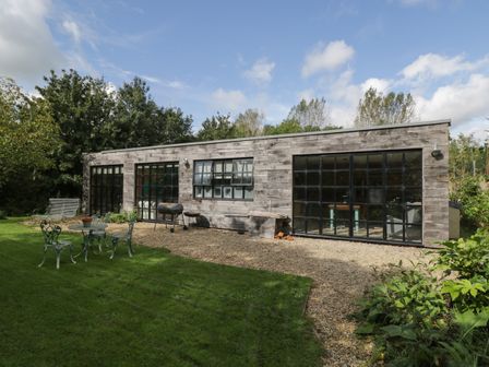 A wooden building with large windows in a garden with metal table and chairs and a green lawn at The Big Box Brandeers Brandier near Minety