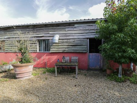 An outdoor area with a wooden table and two chairs in front of a wooden building with a blue door and plants in pots at Brandeers Studio Brandier near Minety