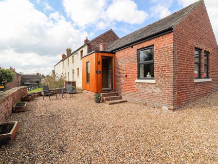 An outdoor patio area with gravel ground a small table with two chairs and a brick building at The Flat in Burgh By Sands