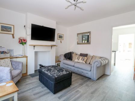 A living room with a gray sofa an armchair a patterned ottoman a wall-mounted TV and a mirror at Donny's Plaice in Caister-On-Sea