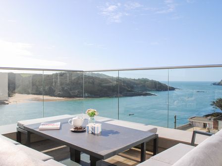 A balcony with a table cups teapot flowers and book overlooking a sea and hills at 3 Hamstone Court in Salcombe