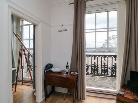 A room with a small wooden table holding a bottle of wine glasses and a plate beside a window with curtains and a telescope near another window at The Seahome in Scarborough