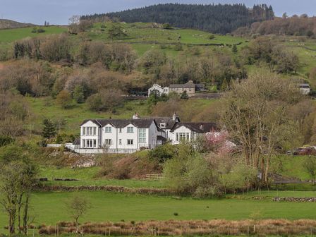 A large white house with green fields and trees on a hillside at Chase View in Bowland Bridge near Bowness-On-Windermere
