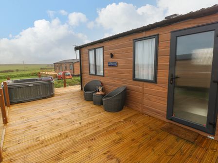 An outdoor wooden deck with two chairs a small table and a hot tub at The Waves in Little Haven near Broad Haven